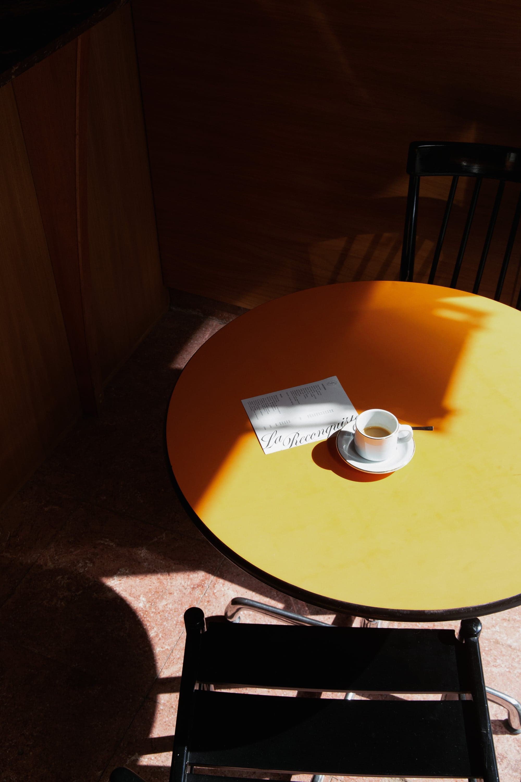 Vista desde arriba de una mesa al sol con un café en taza de borde dorado y la carta impresa